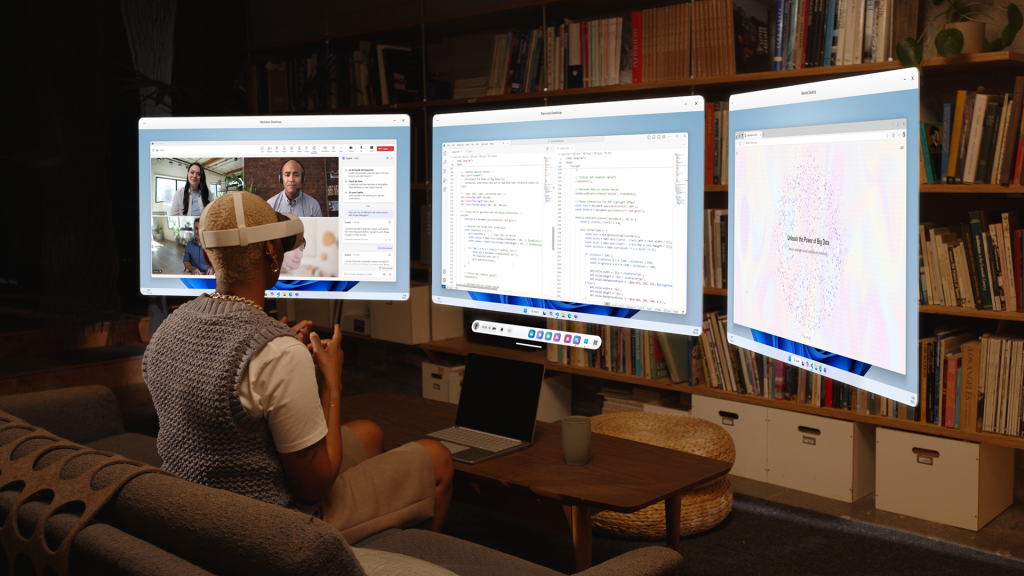 A person wearing a Meta Quest 3S mixed reality headset sits on a couch in a living room, interacting with three large virtual monitors floating in front of them. The monitors display a video conference, a coding editor, and a data visualization webpage. A laptop and a coffee cup are on the wooden coffee table in front of them, with a bookshelf in the background.